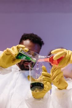 personne portant gants épais et lunettes de protection en train de verser lentement de l'acide dans un seau d'eau à côté d'une piscine