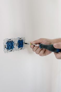 main d'un électricien raccordant des fils électriques colorés sur les bornes à vis d'une prise murale, boîtier d'encastrement visible dans le mur