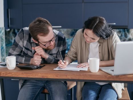 couple assis à une table avec des documents financiers et une calculatrice, en train d'étudier un tableau de simulation de prêt sur un écran d'ordinateur portable