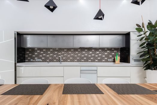 cuisine ouverte lumineuse avec crédence en carrelage blanc, îlot central en bois clair et suspensions noires au-dessus du plan de travail