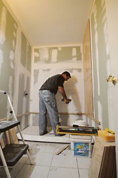 artisan plaquiste posant du placo dans une salle de bain en rénovation, mètre ruban à la main, carrelage encore empilé au sol