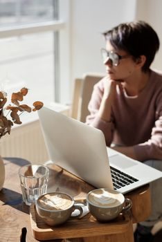 personne assise à un bureau devant un ordinateur portable affichant une carte immobilière avec des points d'annonces, tasse de café à côté, lumière naturelle du matin