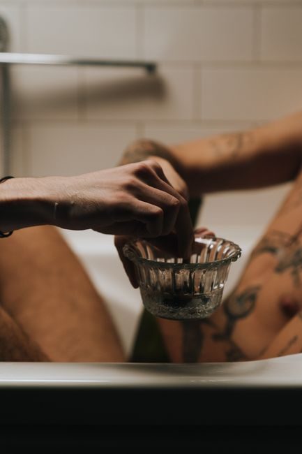 gros plan sur des mains appliquant un dégraissant avec un chiffon sur un joint de silicone blanc autour d'une baignoire, lumière naturelle de salle de bain