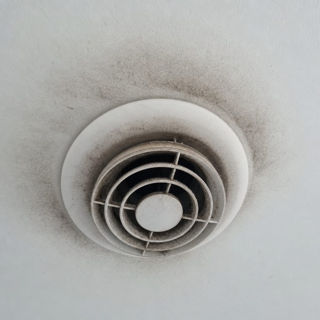 bouche de VMC ronde encrassée avec des traces noires sur le plafond blanc autour de la grille