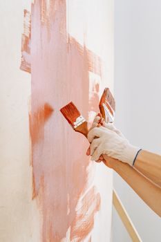 gros plan sur des mains en gants appliquant au pinceau un enduit hydrofuge blanc sur le bas d'un mur en parpaing, à l'extérieur en journée